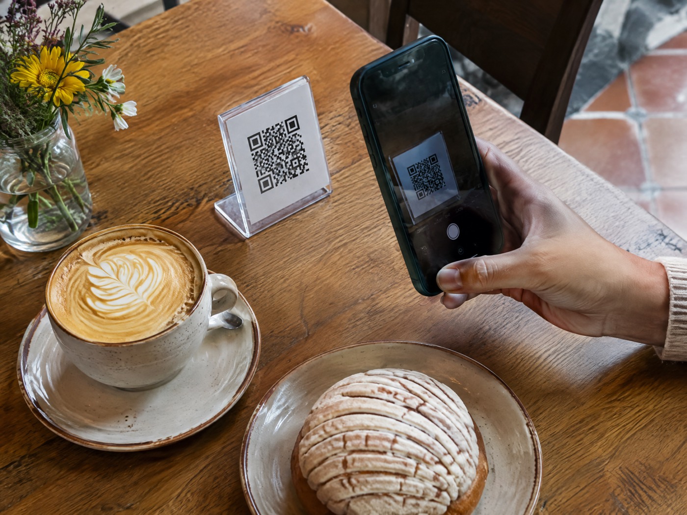 Mesa de cafetería con un código QR, un café y un celular escaneándolo